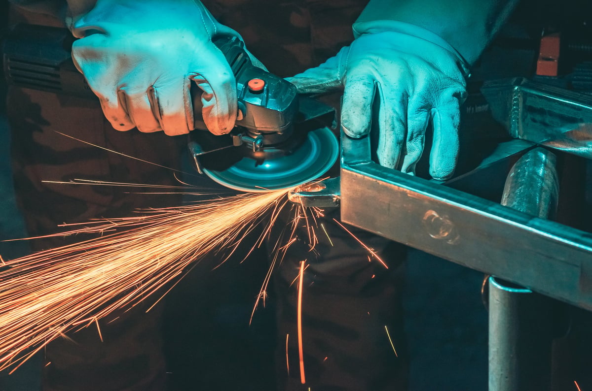 Hands of craftsman in protective gloves with grinding machine on dark background. Golden sparks from grinding metal in workshop. Metalworking.